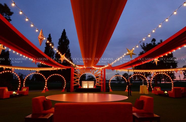 an outdoor wedding venue with red and orange draping, white lights and chairs