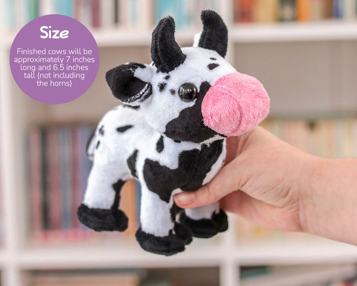 a hand holding a small stuffed cow in front of a bookshelf