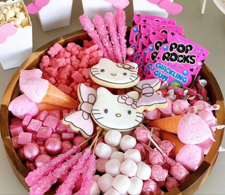 a bowl filled with marshmallows, candies and hello kitty cookies on sticks