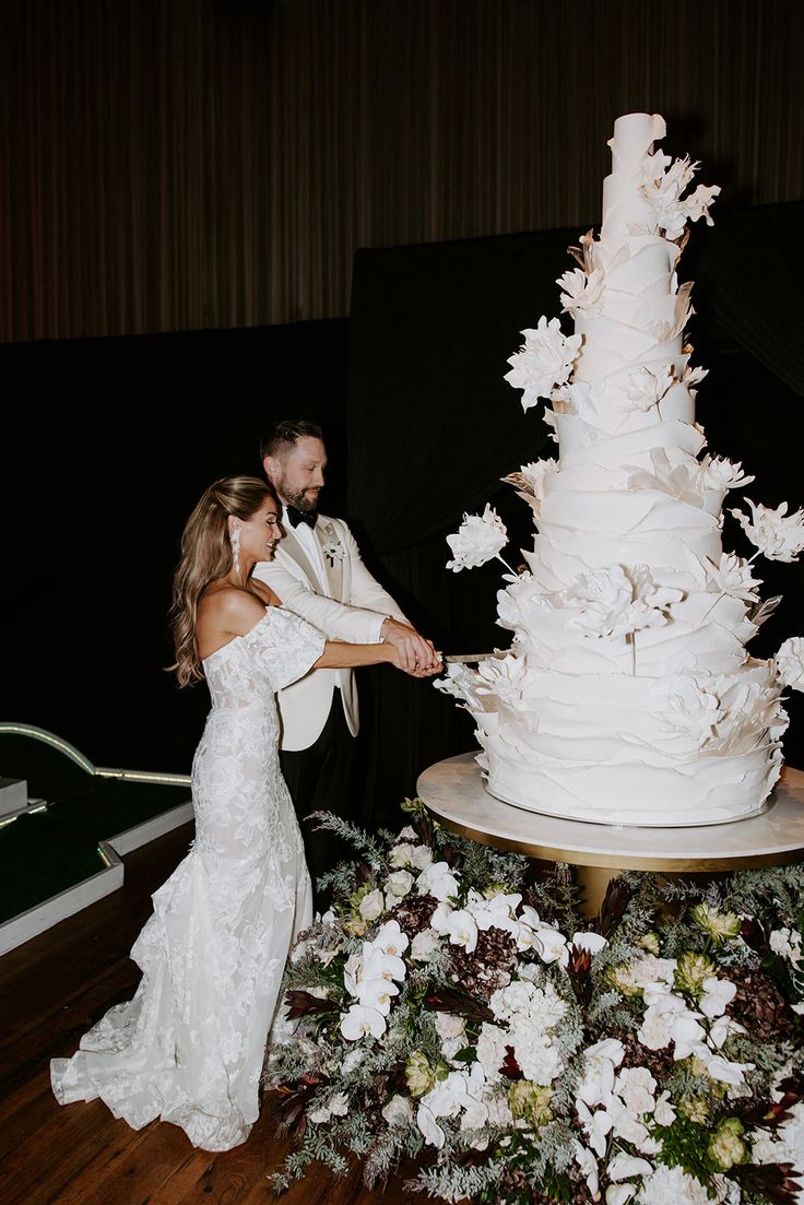 a bride and groom are cutting into a wedding cake with white flowers on the table