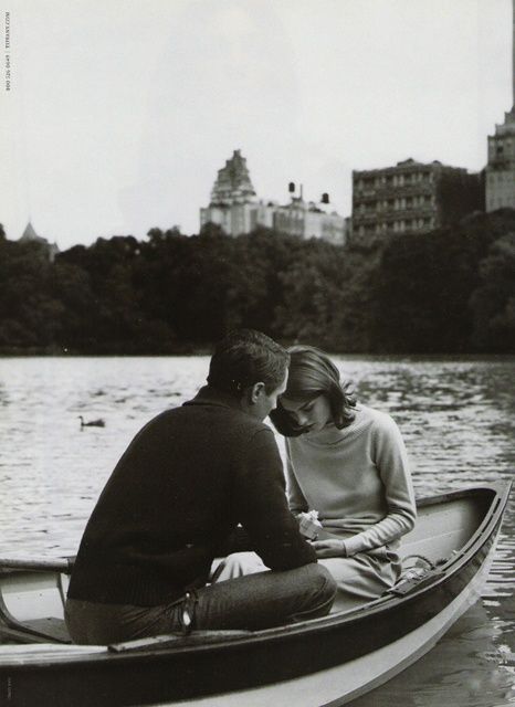 a man and woman sitting in a boat on the water with buildings in the background