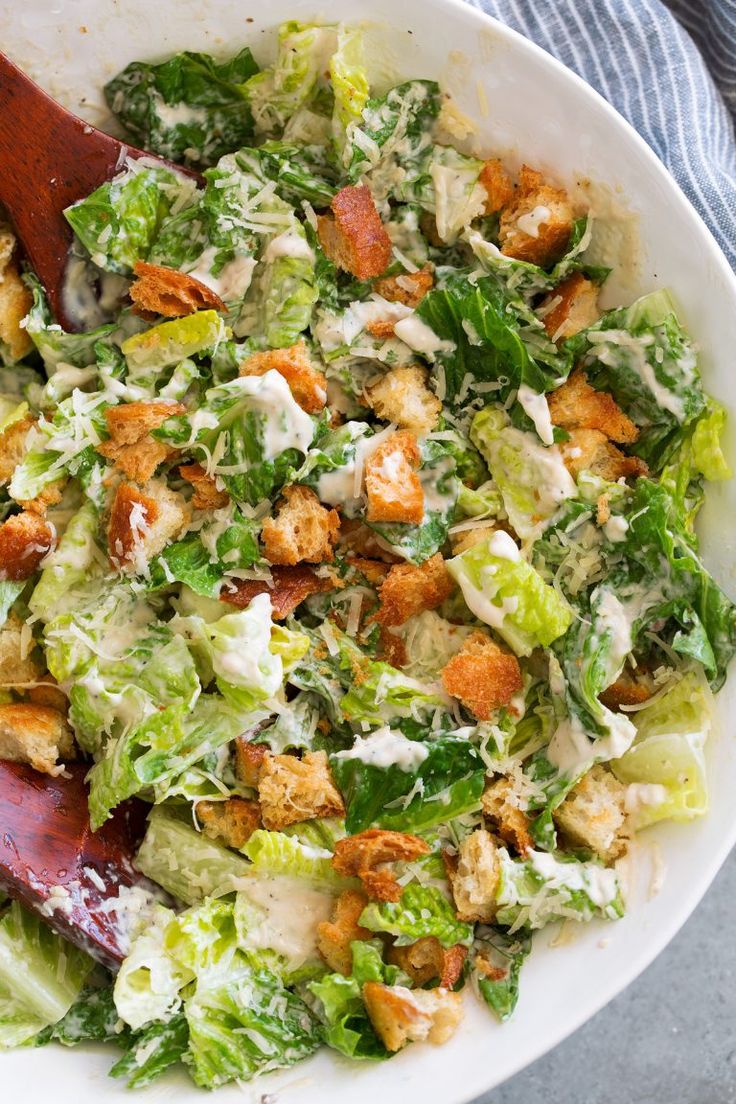 a salad with lettuce, croutons and dressing in a white bowl