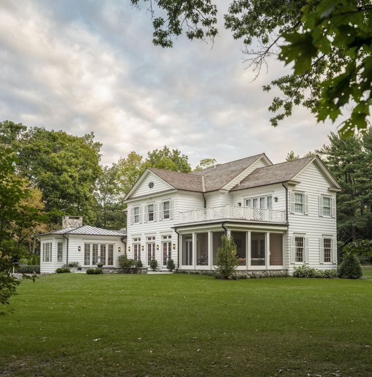 a large white house sitting in the middle of a lush green field with lots of trees