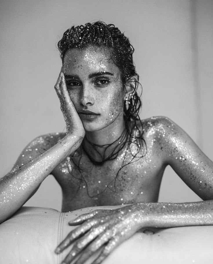 a woman covered in silver glitter sitting on top of a white bed with her hands near her face