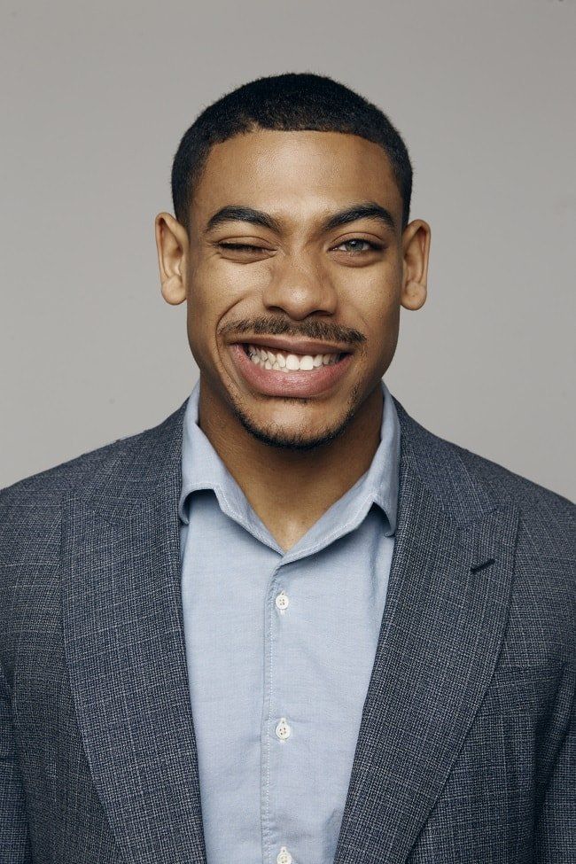 a man in a suit smiling at the camera with a smile on his face while wearing a blue shirt and gray blazer