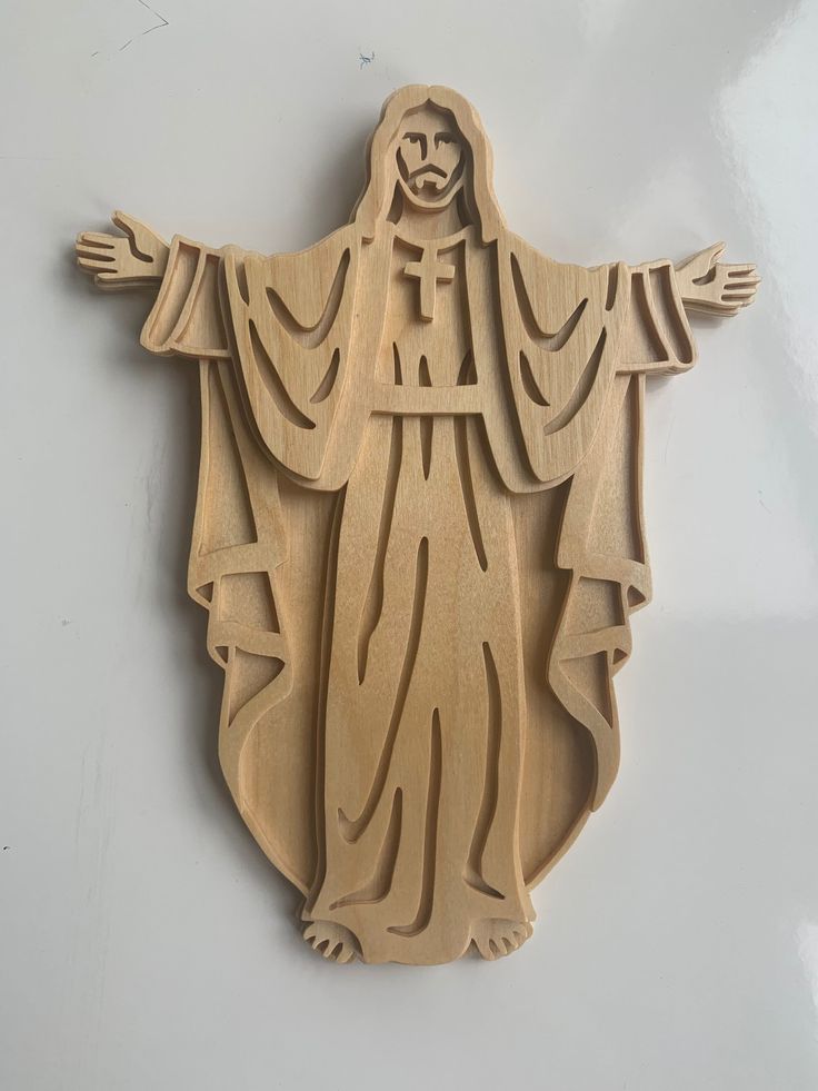 a wooden carving of the statue of jesus on a white surface with his arms outstretched