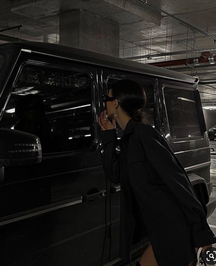 a woman standing next to a black van in a parking garage with her hand on the door