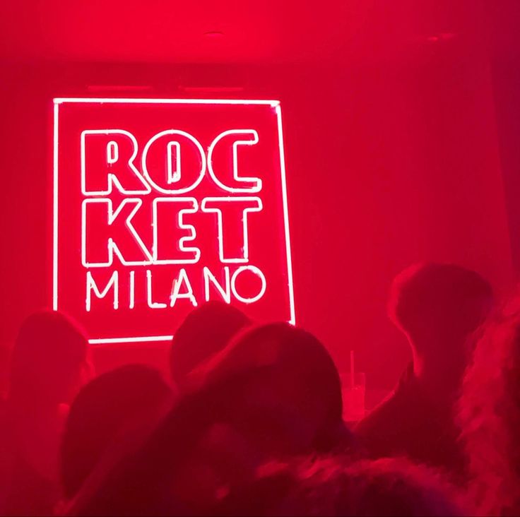 a red neon sign that reads rock ket milano in front of a group of people