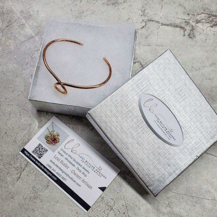 an open box with a gold bracelet on it and a business card in the front