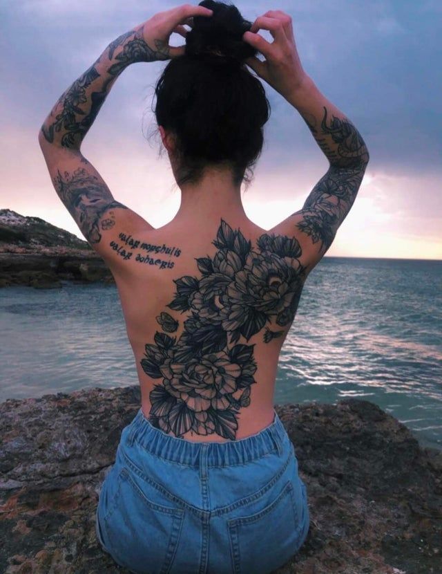 a woman sitting on top of a rock near the ocean with her back to the camera