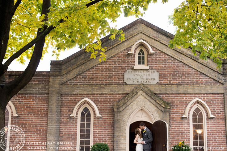 a bride and groom standing in the doorway of a brick church with trees around them