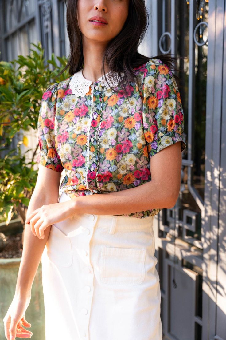 This top is expertly crafted with Liberty Fabrics, ensuring both quality and style. Its cream base color is elevated by a navy blue and multicolored floral print overlay. With a round neckline, eyelet lace collar, and short puff sleeves featuring button cuffs, this blouse is both feminine and functional. The button-down bodice and key hole button detailing on the back add extra charm. Available in sizes XXS, XS, S, M, L, XL, 1X, 2X, 3X, 4X, + 5X!! floral blouse, plus size fashion, floral shirt Spring Crew Neck Blouse With Floral Print, Summer Blouse With Peter Pan Collar And Lace Trim, Short Sleeve Printed Blouse For Garden Party, Printed Short Sleeve Blouse For Garden Party, Spring Floral Print Crew Neck Blouse, Spring Daywear Tops With Peter Pan Collar, Fitted Short Sleeve Blouse For Garden Party, Feminine Multicolor Short Sleeve Blouse, Vintage Crew Neck Blouse For Spring