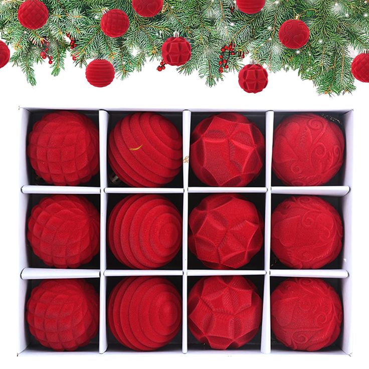 twelve red balls in a white box with christmas decorations hanging from the tree behind them