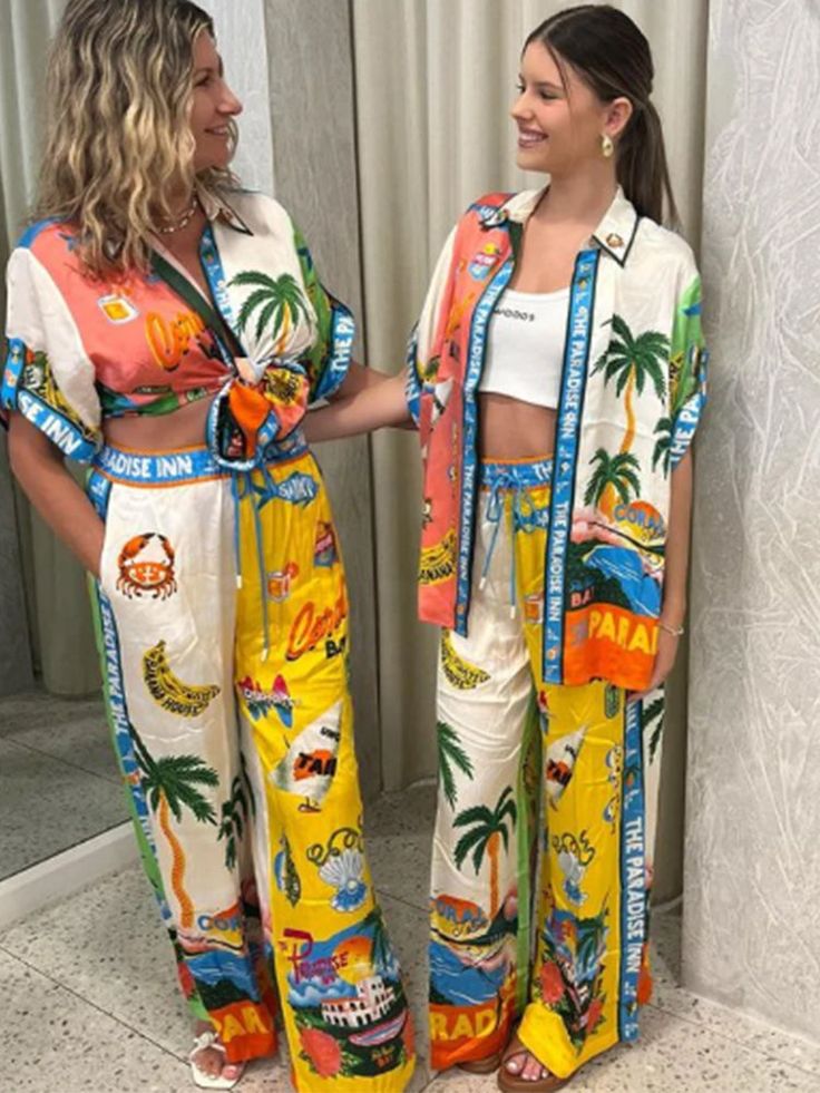 two women standing next to each other wearing matching outfits with palm trees on the side