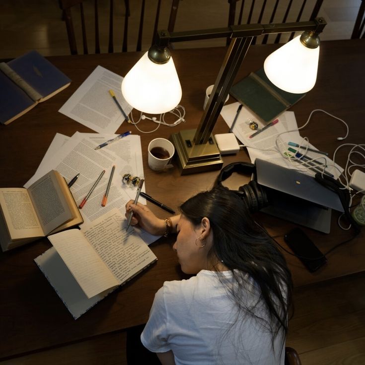 a woman is sitting at a table with many books and writing utensils on it