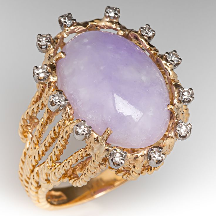 This lavender jade ring features rope details and is centered with a lavender jadeite jade oval cabochon, weighing an estimated 10.41 carats, in a four-prong setting. The center is surrounded by twelve (12) round single cut diamonds in four-prong settings. The ring measures 24.2mm at the top, rises 12.4mm above the finger, tapering to 2.9mm wide and 1.1mm thick at the base of the shank. It is currently a size 7.25. Lavender Jade Ring, Lavender Jade, Ruby Birthstone, Diamond Cocktail Ring, Jewelry Accessories Ideas, Diamond Cocktail Rings, Jade Ring, Accessories Ideas, Ruby Jewelry