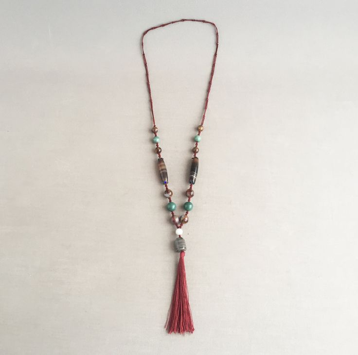 A beautiful oriental necklace consisting of several  semi precious polished stone beads including Jade and Tigers eye. Held on a burgandy hand knotted silk cord and ending in a silk tassel. Pleasingly weighty, A truly beautiful piece to wear and display. Supplied in a gift box Jade has long been considered to be a lucky stone Green Jade is believed to bring tranquility to the spirit and calm wisdom to the mind. Tigers Eye is a crystal with lovely bands of yellow-golden colour through it. A power Adjustable Spiritual Tassel Necklaces, Spiritual Tassel Necklaces With Adjustable Fit, Bohemian Hand Knotted Necklace For Rituals, African Beads Necklace, Tube Necklace, Golden Colour, Lucky Stone, Silk Cord, African Beads