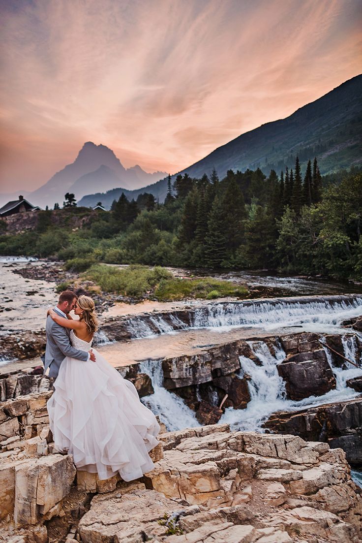 a bride and groom standing on the edge of a waterfall