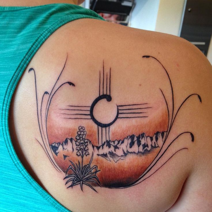 a woman with a tattoo on her shoulder has a sunset and mountains in the background