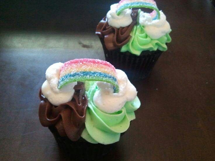 two cupcakes with green frosting and a rainbow decoration on the top one