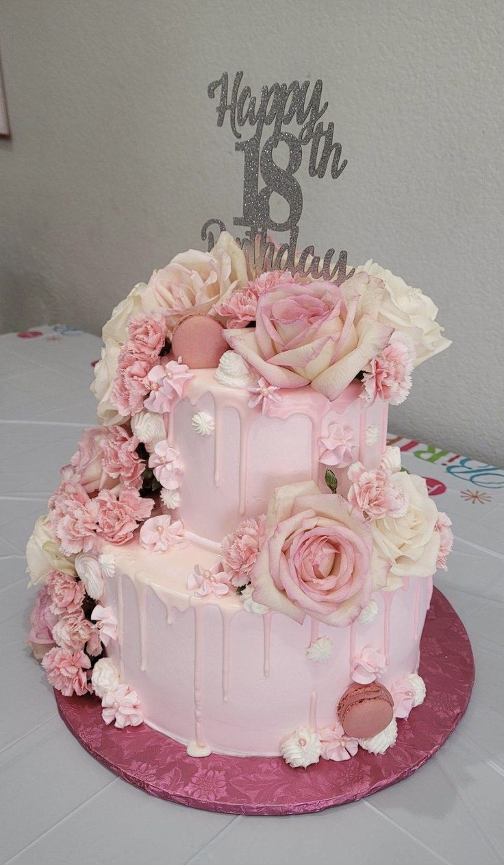 a three tiered cake with pink flowers and silver happy 18th birthday sign on top