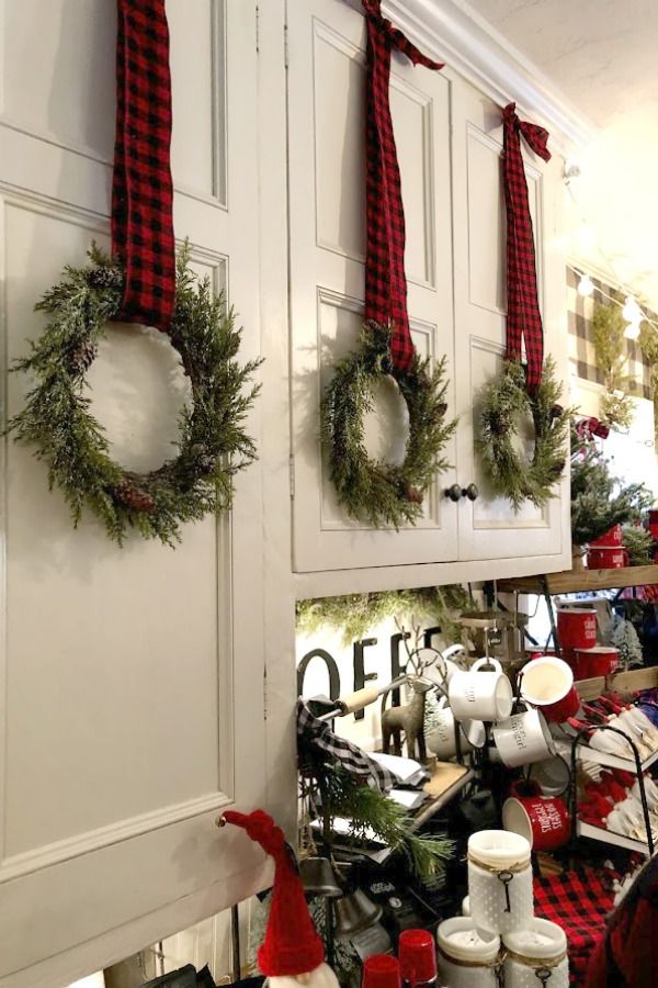 christmas wreaths hang on the wall in front of white cabinets with red and black plaid ribbon