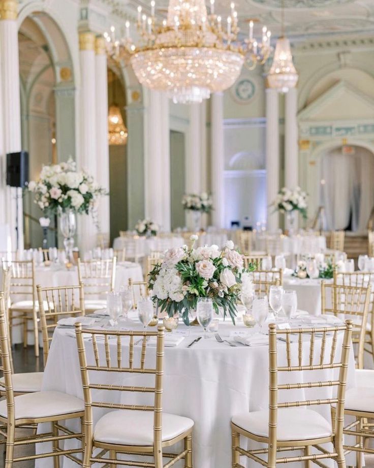 the tables are set with white flowers and gold chairs