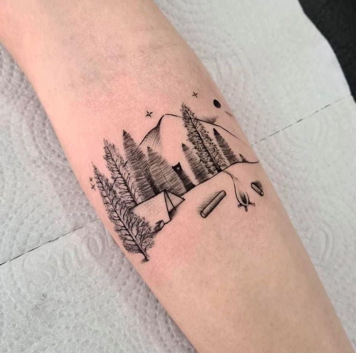 a person with a tattoo on their arm that has trees and mountains in the background