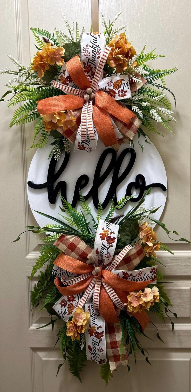 a door hanger that says hello with orange and white bows on it, hanging from the front door