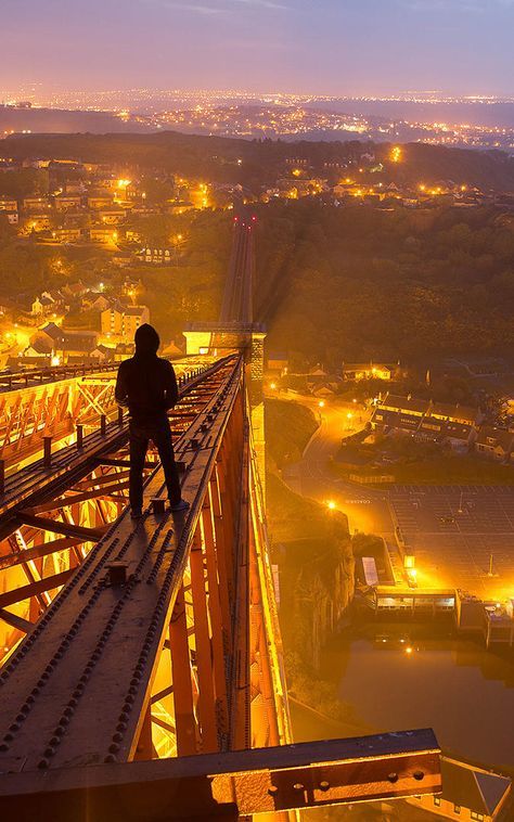 a man standing on the edge of a bridge at night looking out over a city