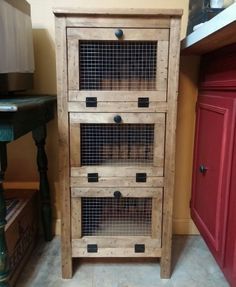 a small wooden cabinet with three drawers and wire doors on the bottom, in front of a red door