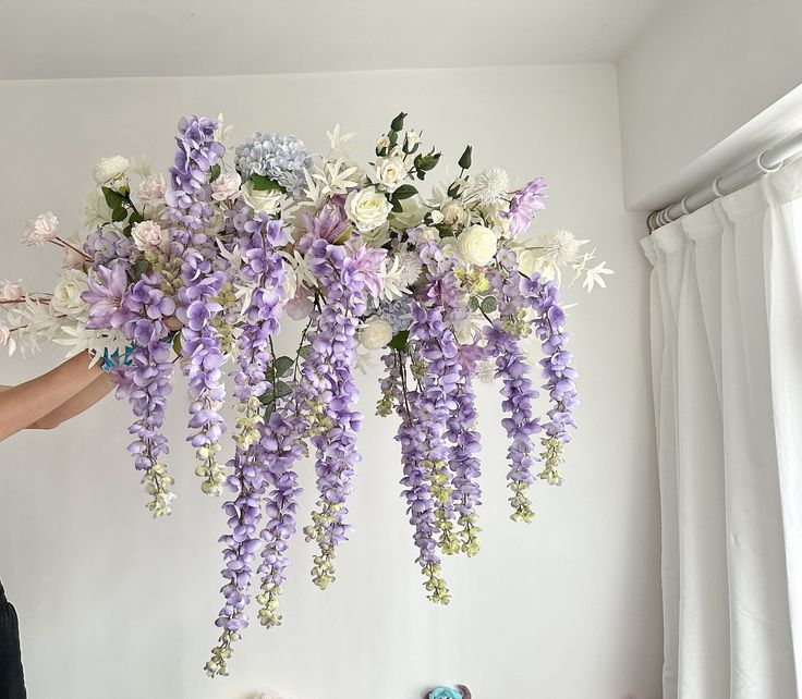 a woman holding a bunch of purple and white flowers in front of a bed with stuffed animals