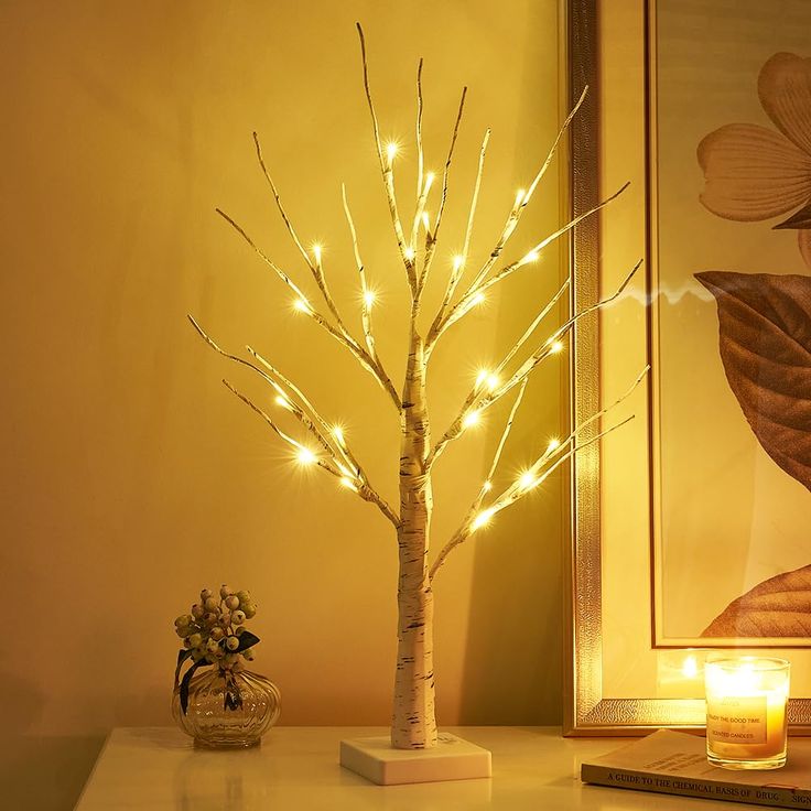 a lighted tree next to a vase with flowers on it and a mirror in the background