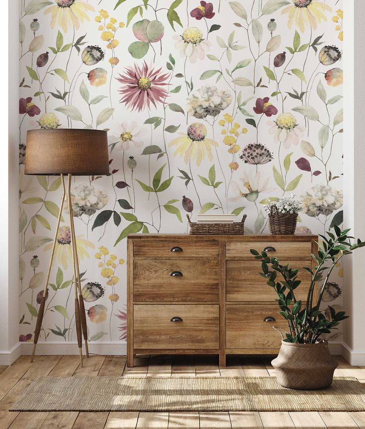 a room with a dresser, lamp and wallpaper that has flowers painted on it