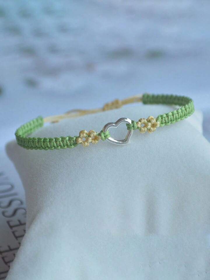 a green and gold bracelet with a silver heart charm on top of a white cloth