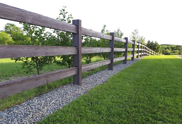 a wooden fence in the middle of a grassy area with gravel and rocks on both sides