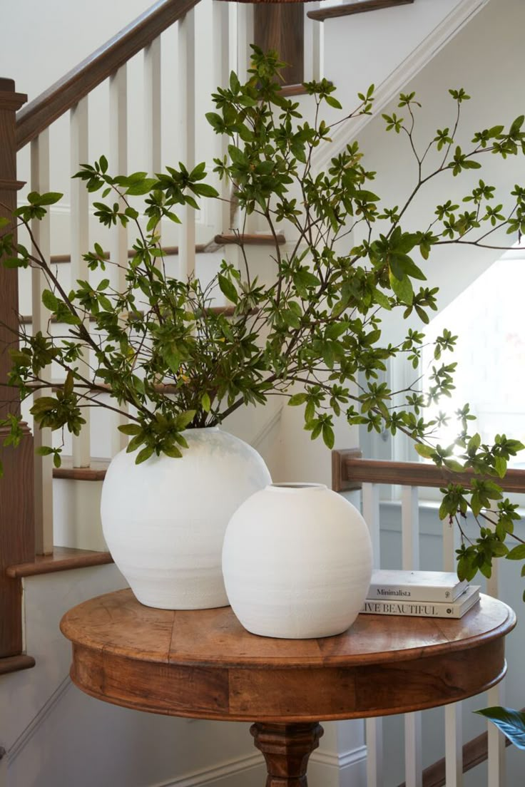 two white vases sitting on top of a wooden table next to a stair case