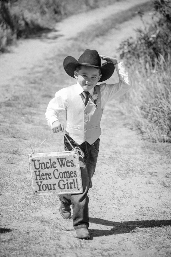 a young boy wearing a cowboy hat and holding a sign that says uncle west here comes your girl