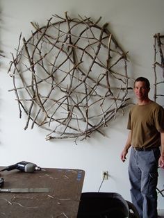 a man standing in front of a wall sculpture made out of sticks and branches,