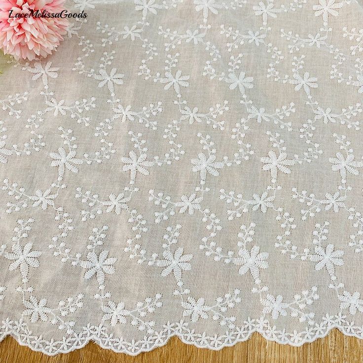 the table cloth has white lace on it and is next to a pink flower in a vase