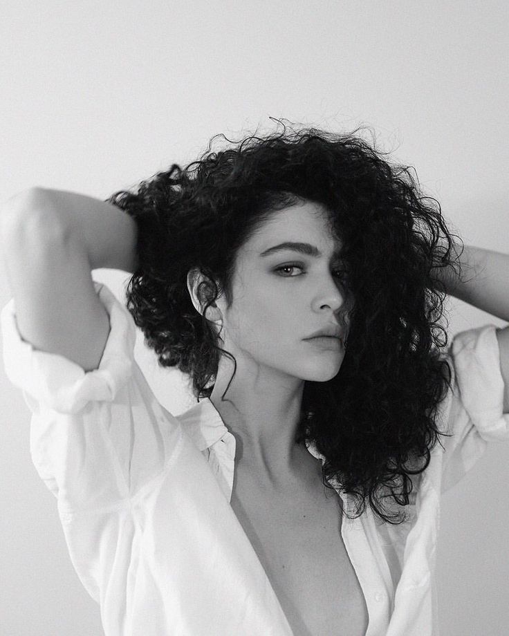 a black and white photo of a woman with curly hair wearing a shirt over her shoulder