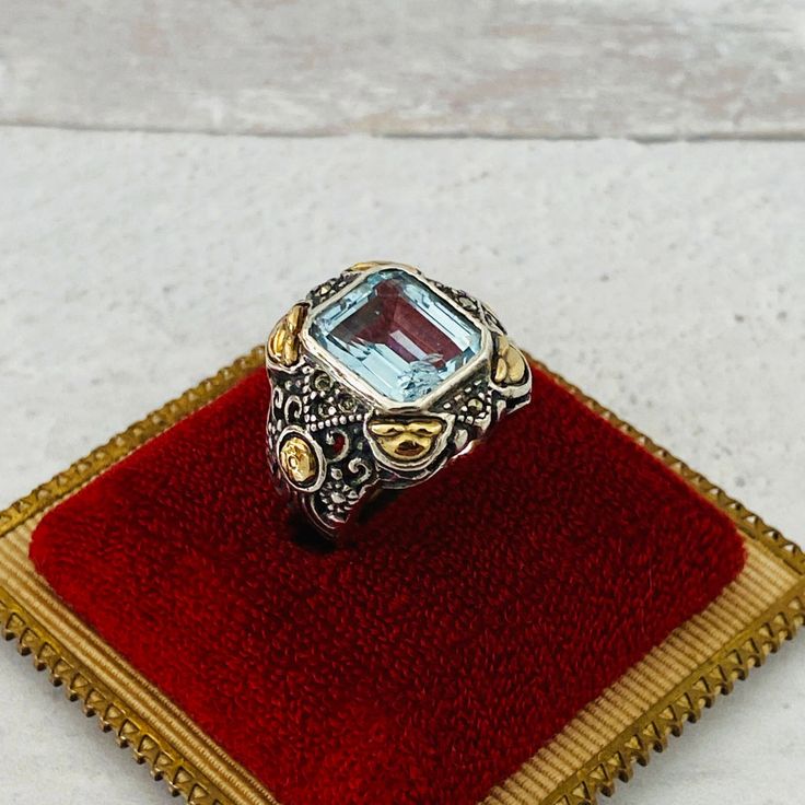 Vintage Swiss Blue Topaz 18k Gold Sterling Silver Ring 8 ct Gem Fashioned in solid sterling silver with applied 18k gold accents, this ring is set with a gorgeous genuine emerald cut Swiss blue topaz gem.  There are marcasites above and below the main stone. The shoulders are carved in an intricate scroll pattern. The setting measures 3/4" or 19mm north-south. The east-west measurement for the bezel setting is approximately 11/16" or 17mm. The lovely baby blue topaz is estimated to measure 12mm Scroll Pattern, Maker’s Mark, North South, Swiss Blue Topaz, East West, Bezel Setting, Emerald Cut, Gold Accents, Sterling Silver Ring