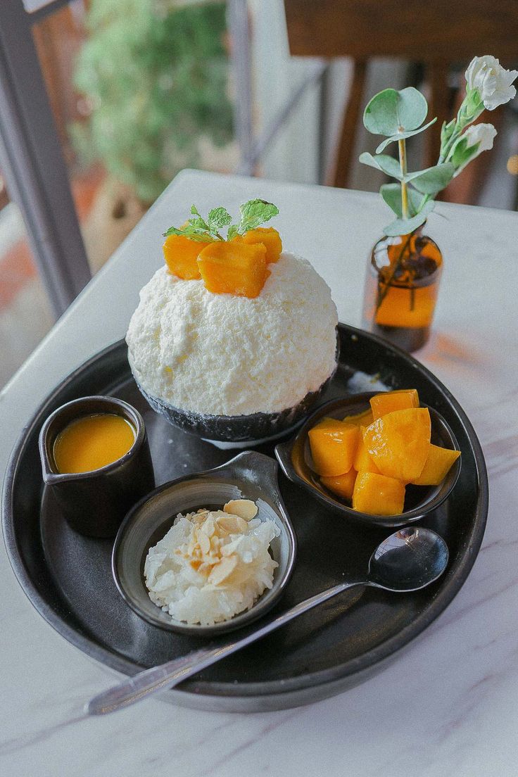 a black plate topped with rice and fruit on top of a white table next to two cups