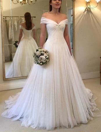 a woman standing in front of a mirror wearing a wedding dress with off the shoulder sleeves