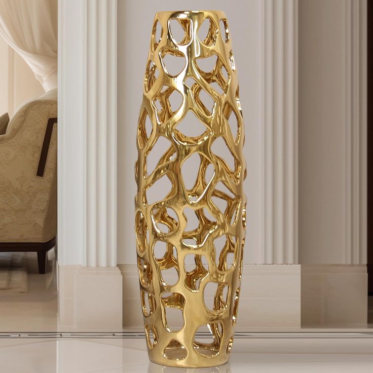 a gold vase sitting on top of a white floor next to a chair and table