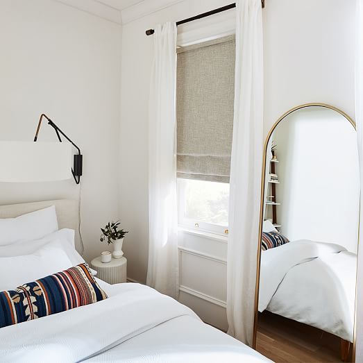 a bedroom with a bed, mirror and window in the corner that has white linens on it