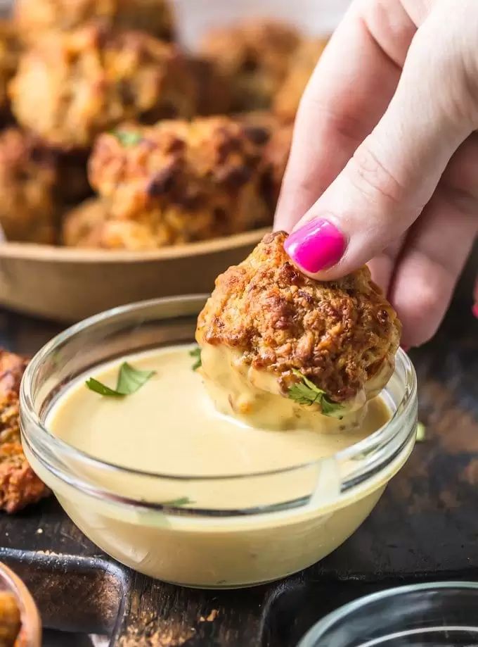 a person dipping something into a small bowl with sauce on it and other food in the background