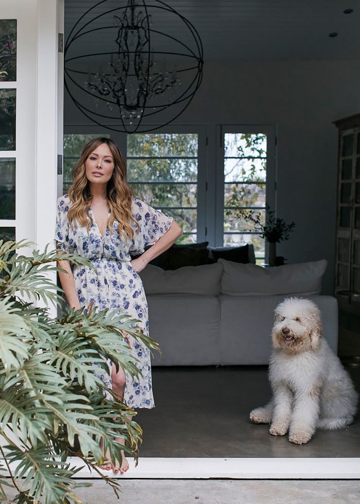 a woman standing next to a white dog in front of a living room filled with furniture