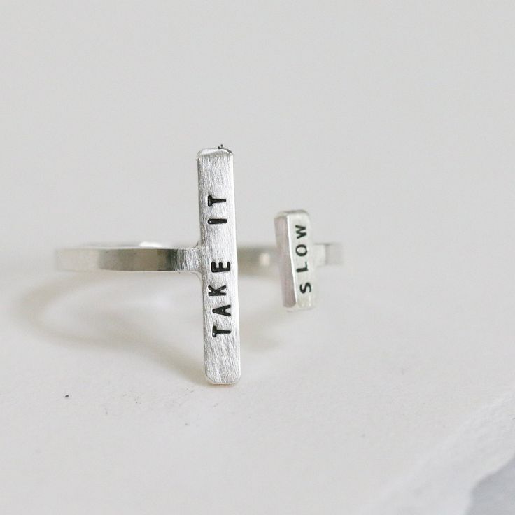 One of our favorite gift-able rings, the Double Adjustable Ring is an eye-catching way to inspire & encourage. An adjustable, asymmetric ring with a tiny phrase of inspiration. Letters are individually stamped by hand, making each ring one of a kind. The message is centered on each bar in our signature teeny-tiny uppercase block font. For an unconventional look, try stacking with our diamond dusted adjustable rings. details+ longer bar measures 5/8" wide x 2 mm tall+ shorter bar measures 1/4" wi Inspirational Adjustable Ring, Adjustable Inspirational Sterling Silver Rings, Inspirational Adjustable Sterling Silver Rings, Adjustable Inspirational Rings For Everyday, Adjustable Sterling Silver Stackable Rings, Custom Text Adjustable Sterling Silver Jewelry, Modern Personalized Adjustable Stackable Rings, Adjustable Hand Stamped Midi Rings As Gifts, Adjustable Open Ring With Meaningful Style