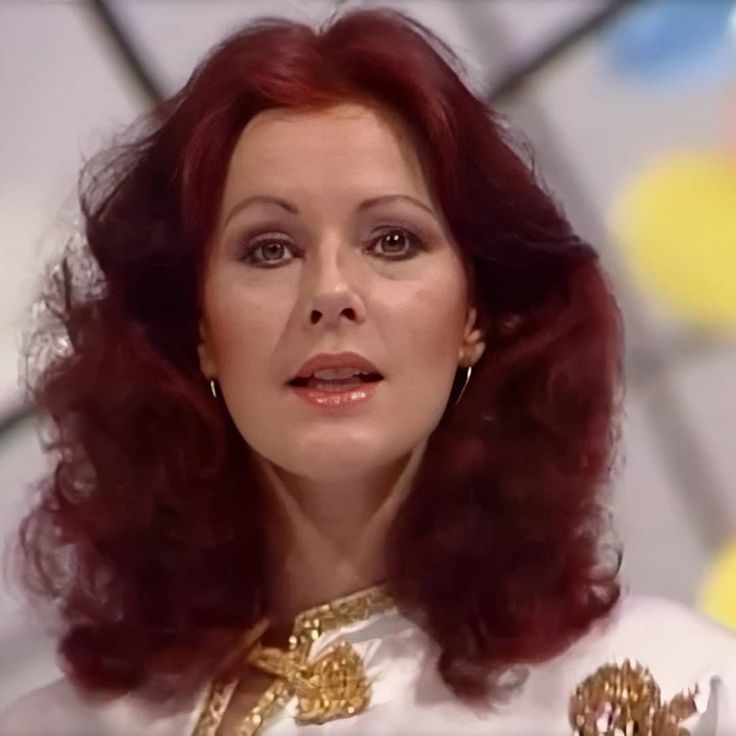 a woman with red hair wearing a white dress and gold jewelry on her neck is looking off to the side